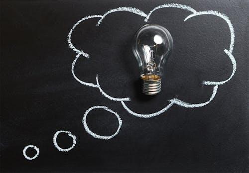 Free Light bulb laying on chalkboard with drawn thought bubble, symbolizing creative ideas. Stock Photo